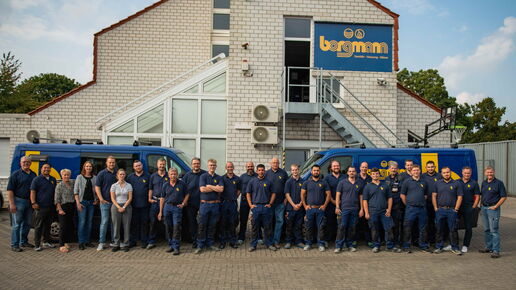 Gruppenfoto des gesamten Borgmann-Teams in Arbeitskleidung vor dem Firmengebäude mit zwei blauen Firmenfahrzeugen.