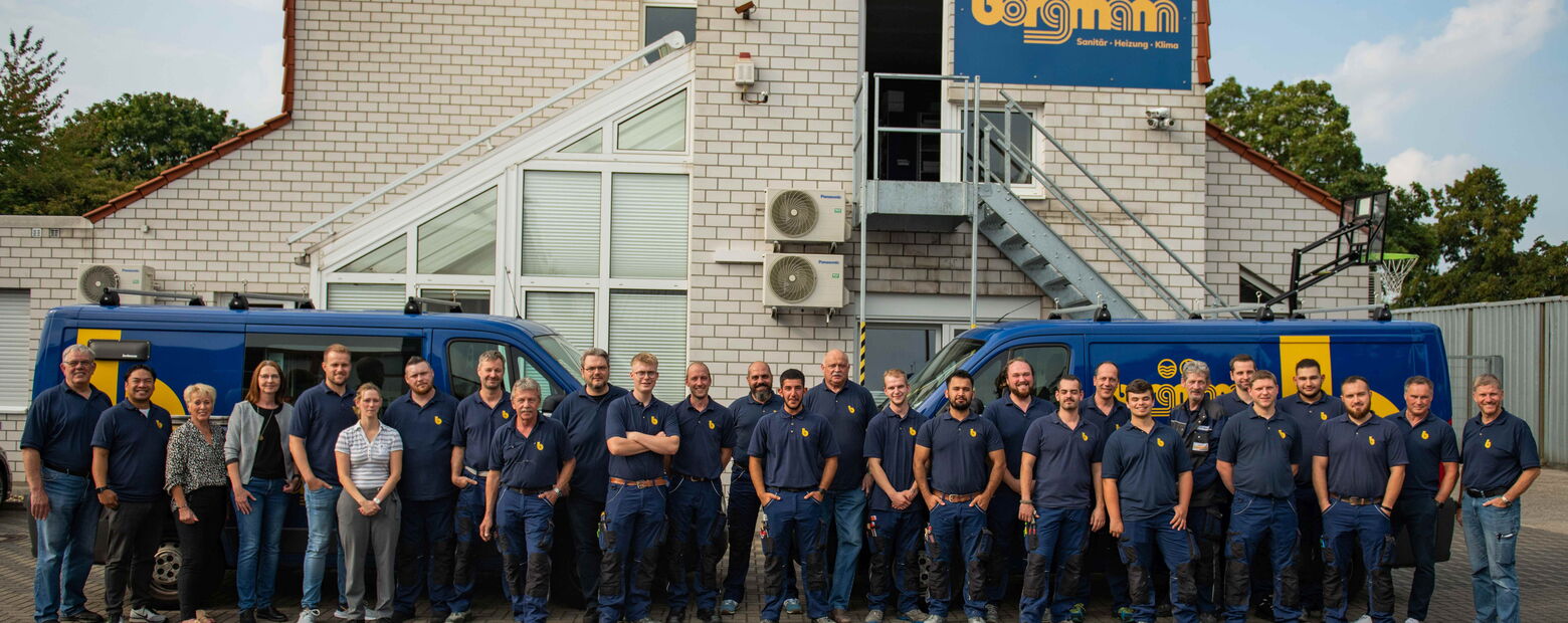 Gruppenfoto des gesamten Borgmann-Teams in Arbeitskleidung vor dem Firmengebäude mit zwei blauen Firmenfahrzeugen.