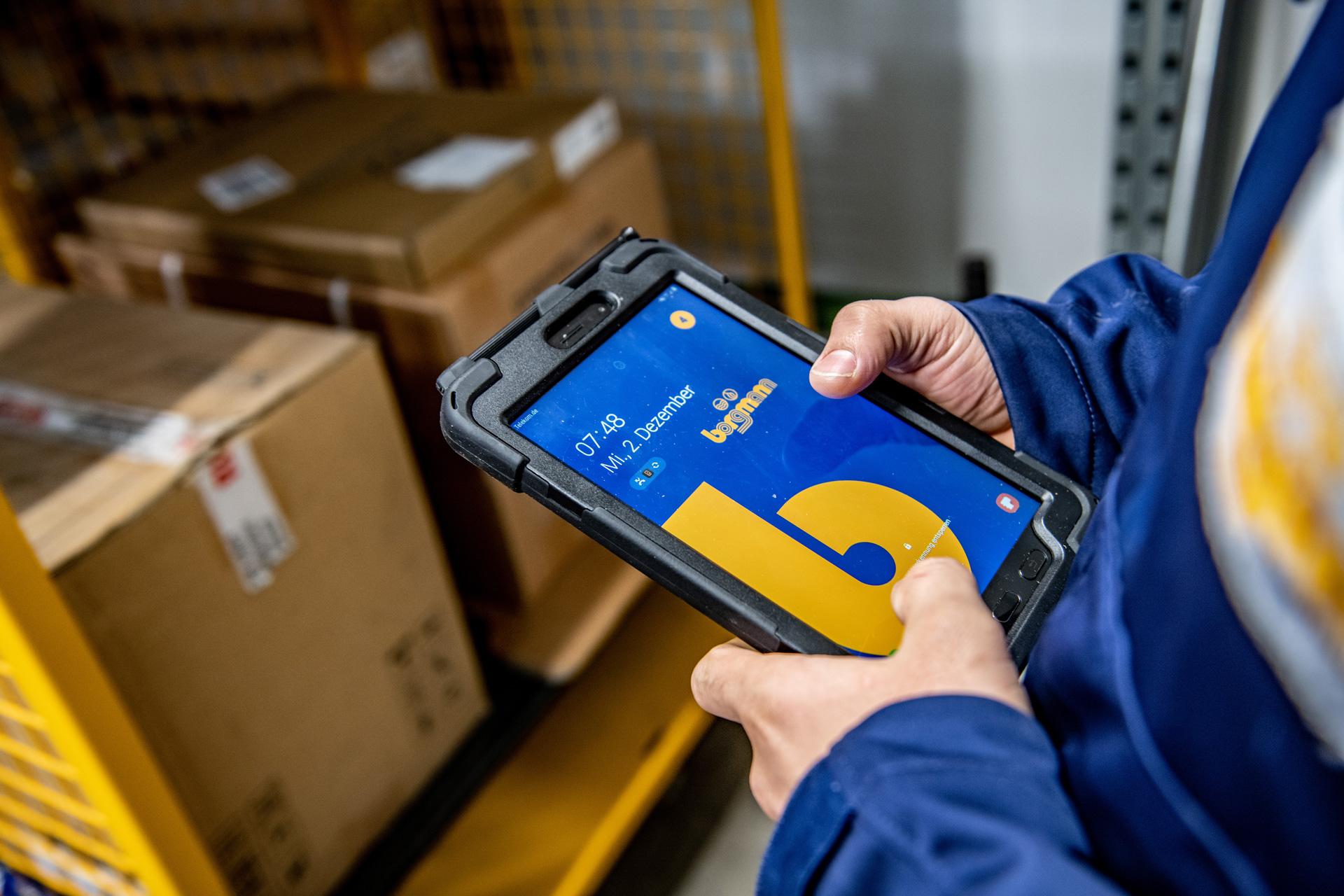 Mitarbeiter hält ein Tablet mit Borgmann-Logo in der Hand, im Hintergrund Kartons und Regale im Lagerbereich.